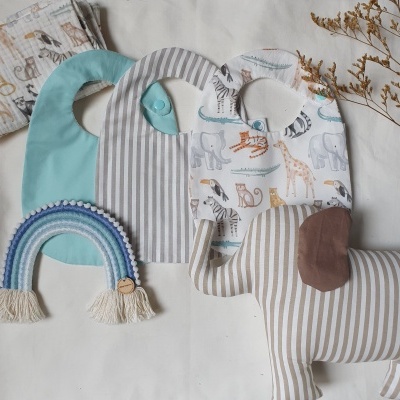 Três babetes infantis com desenhos e riscas, arco-íris de croché e brinquedo elefante riscado