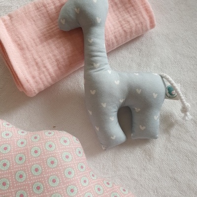 Pelúcia girafa azul com corações brancos, manta rosa e almofada com padrão rosa e verde