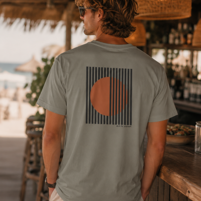 Homem de costas com t-shirt cinza clara com estampa geométrica laranja e preta em bar de praia