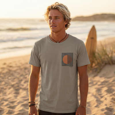 Homem com t-shirt cinza clara com estampa preta e laranja numa praia durante o entardecer