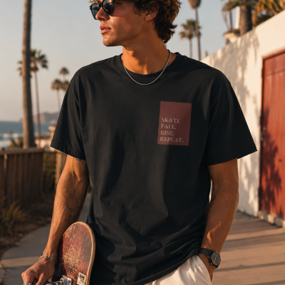 Homem com t-shirt preta e mensagem SKATE FALL. RISE. REPEAT. segurando skate junto a palmeiras