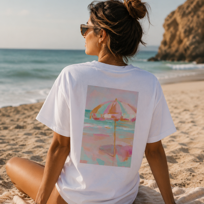 Mulher sentada na praia com t-shirt branca estampada de guarda-sol colorido.
