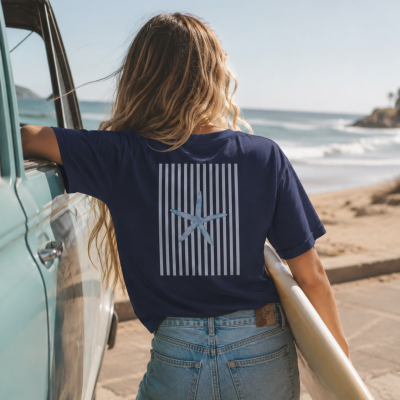 T-shirt azul com estampa de estrela-do-mar sobre faixas verticais brancas nas costas, calças de ganga azuis e pessoa junto a veículo e praia.