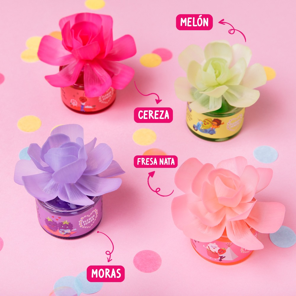 The Fruit Company - Flor Perfumada Quatro frasquinhos coloridos com flores de tecido e rótulos com nomes de sabores sobre fundo rosa com pontos coloridos