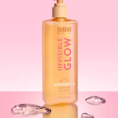 Frasco amarelo com doseador de hidratante para bronzeado sobre fundo rosa e gelo transparente.