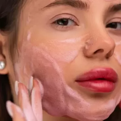 Mulher com espuma rosa no rosto fazendo limpeza facial