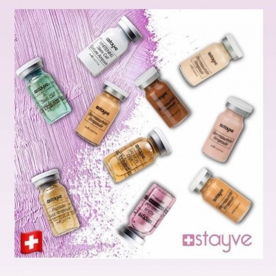 Vários frascos de vidro pequenos de diferentes cores e rótulos STAYVE sobre fundo branco e lilás