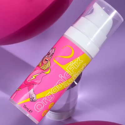 Frasco de creme rosa e amarelo com doseador branco e tampa transparente sobre fundo lilás