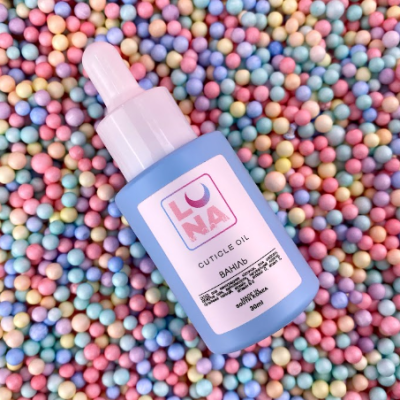 Frasco azul claro de óleo para cutículas LUNA com tampa branca e conta-gotas sobre bolas coloridas