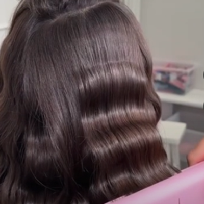 Prancha modeladora cor-de-rosa 'Mamole' ao lado de cabelo castanho ondulado preso com grampo rosa