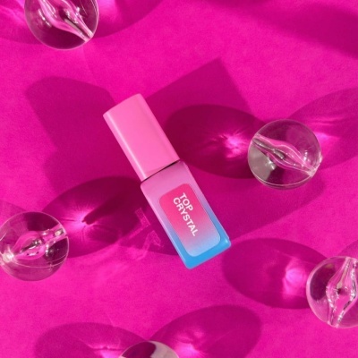 frasco de verniz com tampa rosa e corpo azul e rosa com texto TOP CRYSTAL, rodeado de esferas transparentes em fundo rosa