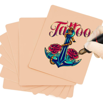 Almofadas para prática de tatuagem com desenho colorido de âncora e rosas, palavra 'Tattoo' e mão com máquina de tatuar