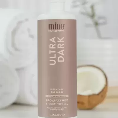 Frasco de produto capilar mine Professional Ultra Dark em superfície branca com toalhas e coco ao fundo