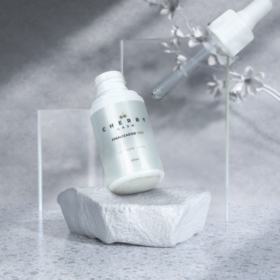 Frasco branco com conta-gotas transparente da marca CHERRY sobre pedra branca e flores desfocadas