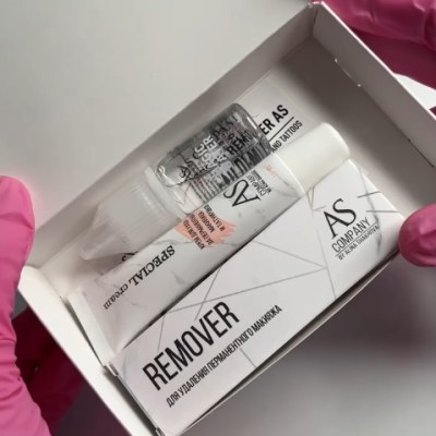 Conjunto de produtos de remoção de tatuagens em embalagem branca, com frasco e tubo, segurado por mãos com luvas cor-de-rosa.
