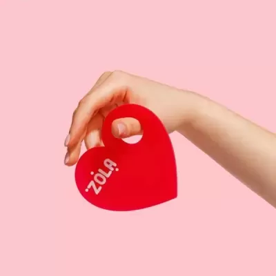 Mão a segurar objeto vermelho em forma de coração com texto ZOLA