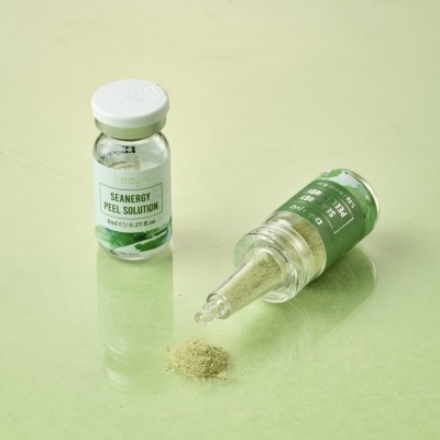 Frascos de vidro com soluções líquidas e rótulos verdes e brancos sobre superfície verde clara