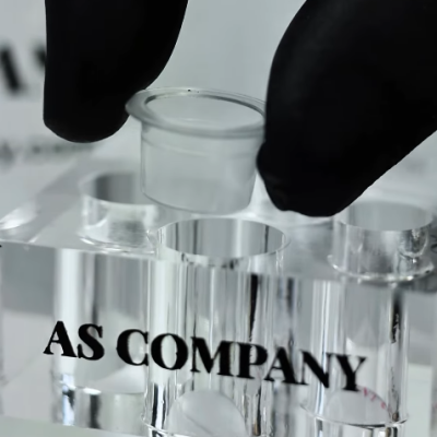 Mão com luva preta segurando tubo plástico transparente sobre suporte acrílico