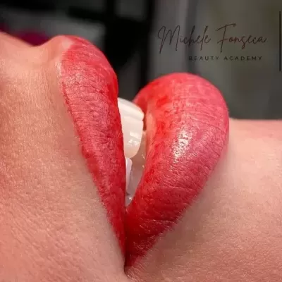 Lábios vermelhos brilhantes com dentes à mostra e texto Michele Fonseca BEAUTY ACADEMY ao fundo