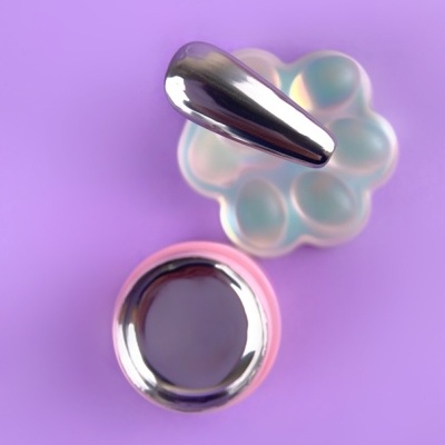 Ponta de unha prateada brilhante sobre paleta opalescente em fundo lilás