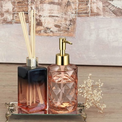 Conjunto de dispensador de sabão rosa e difusor de aroma com varetas sobre tabuleiro espelhado