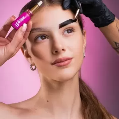 Mulher com sobrancelhas sendo tingidas com produto de frasco rosa