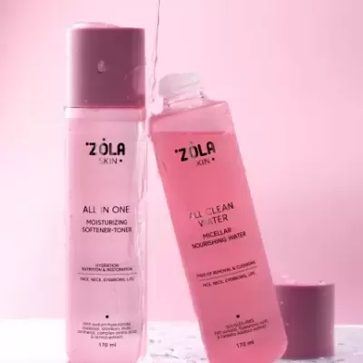 Dois frascos cor-de-rosa de produtos de pele ZOLA SKIN em fundo rosa com gotas de água