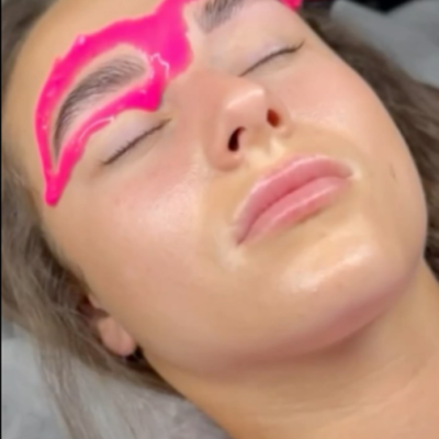 Aplicação de pigmento rosa em gel nas sobrancelhas de mulher com olhos fechados