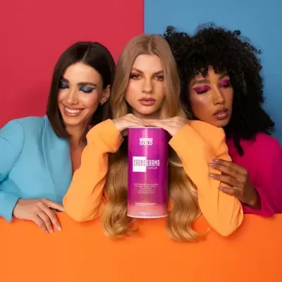 Três mulheres com maquilhagem colorida seguram um recipiente roxo com texto 'GOLD IRONMAMA COLLAGEN'