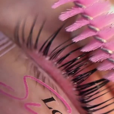 Aplicação de máscara de pestanas com escova rosa e frasco do produto.