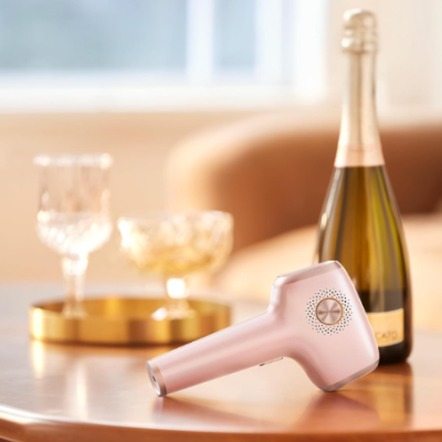 Dispositivo electrónico rosa claro numa mesa de madeira com garrafa de champanhe e copos