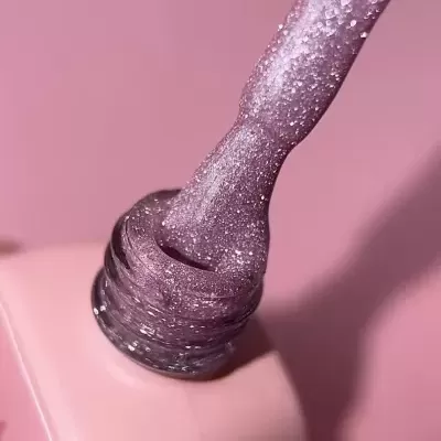 Pincel com verniz de unhas roxo glitterado num frasco rosa claro
