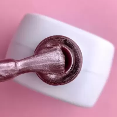 Frasco branco com pincel de esmalte rosa metálico em fundo rosa