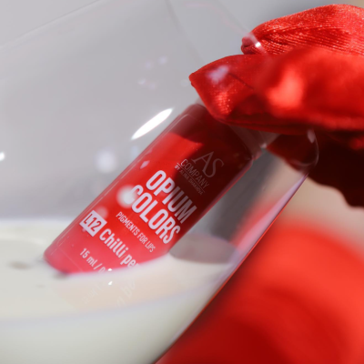 Tubos de tinta vermelho com etiqueta Opium Colors dentro de um copo com líquido branco, segurado por luva vermelha