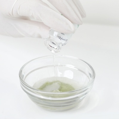 Mão com luva vertendo líquido de frasco para tigela de vidro