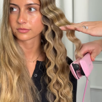 Mulher com cabelo loiro ondulado a ser estilizado com prancha de cabelo rosa