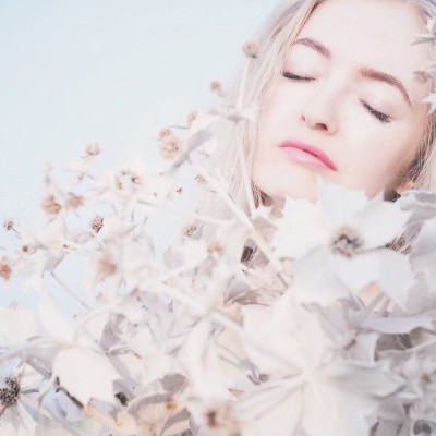 Mulher com olhos fechados rodeada por flores secas claras