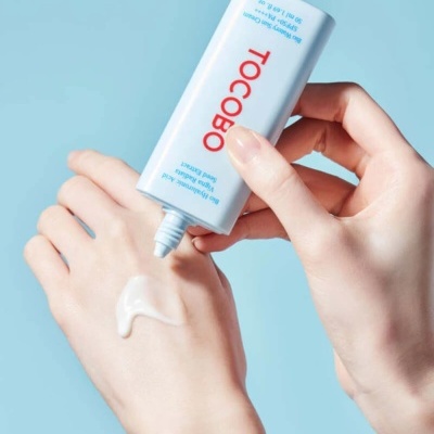 Aplicação de creme TOCOBO em mão com fundo azul claro