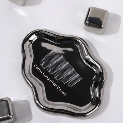 Unhas postiços transparentes em bandeja prateada ondulada com cubos metálicos ao redor