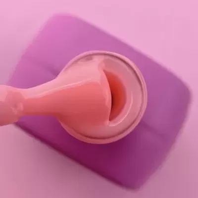 Pincel aplicando verniz cor-de-rosa sobre superfície rosa com objeto lilás ao fundo