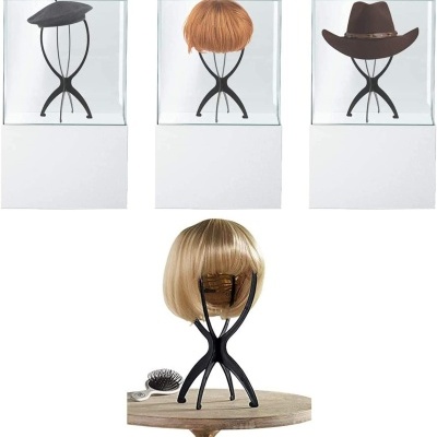 Suportes pretos para chapéus e perucas com design moderno, três dentro de caixas transparentes e um com peruca loira e escova ao lado sobre mesa de madeira.