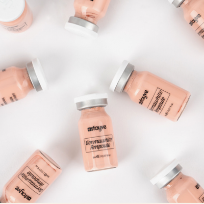 Frascos transparentes de ampoule com líquido cor de pele e tampas brancas, rótulo preto, fundo branco