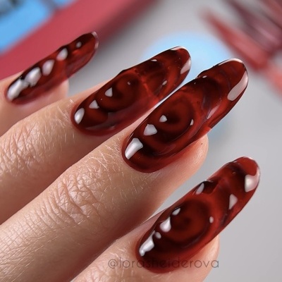 Unhas artificiais vermelhas translúcidas com padrão em espiral e brilho intenso