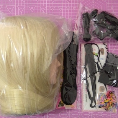 Cabeça manequim loiro claro e acessórios para cabelo variados em mesa rosa quadriculada