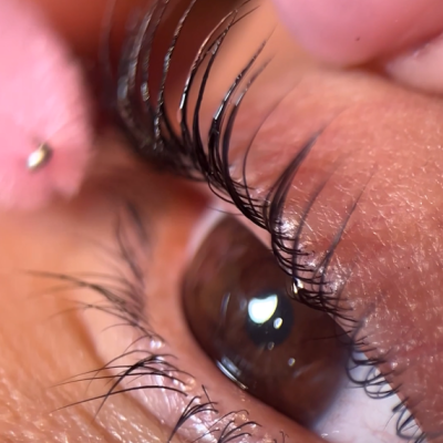 Olho castanho com pestanas e dedo segurando objeto rosa