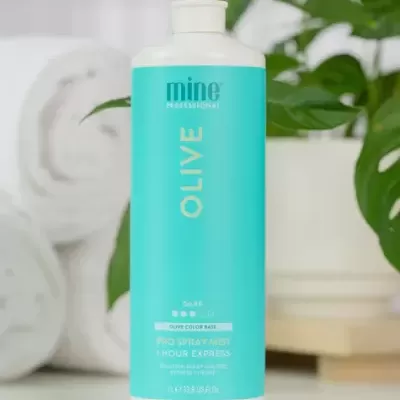 Frasco azul claro de spray de cor Olive com tampa branca em superfície branca, com toalhas brancas e plantas ao fundo