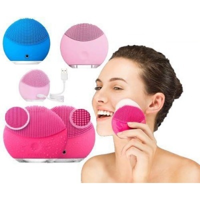 Escovas elétricas de limpeza facial em silicone azul, rosa claro e rosa escuro com cabo USB e mulher usando a escova rosa escura no rosto.