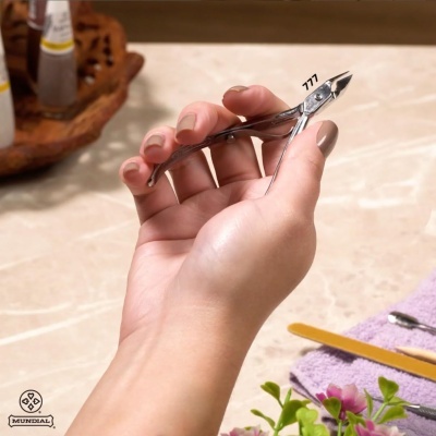 Mão segurando corta-unhas metálico prateado com número 777 em ambiente de manicure