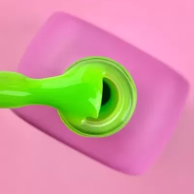 Frasco de verniz verde aberto com pincel sobre fundo rosa