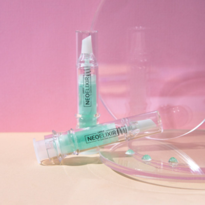 Frascos de plástico transparente com líquido verde azulada etiquetados NEOELIXIR sobre superfície bege e fundo rosa.